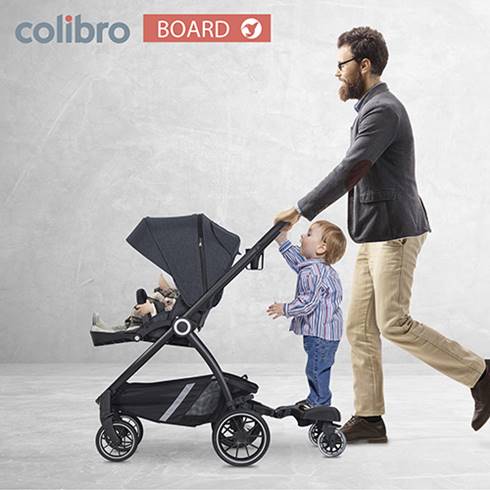 Dziecko stoi na dostawce do wózka Colibro Board, tata prowadzi wózek.